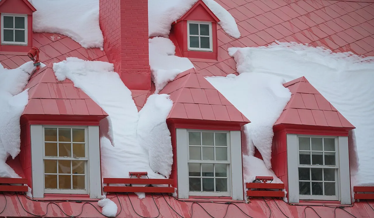 Snow sliding off a red metal roof with three dormers